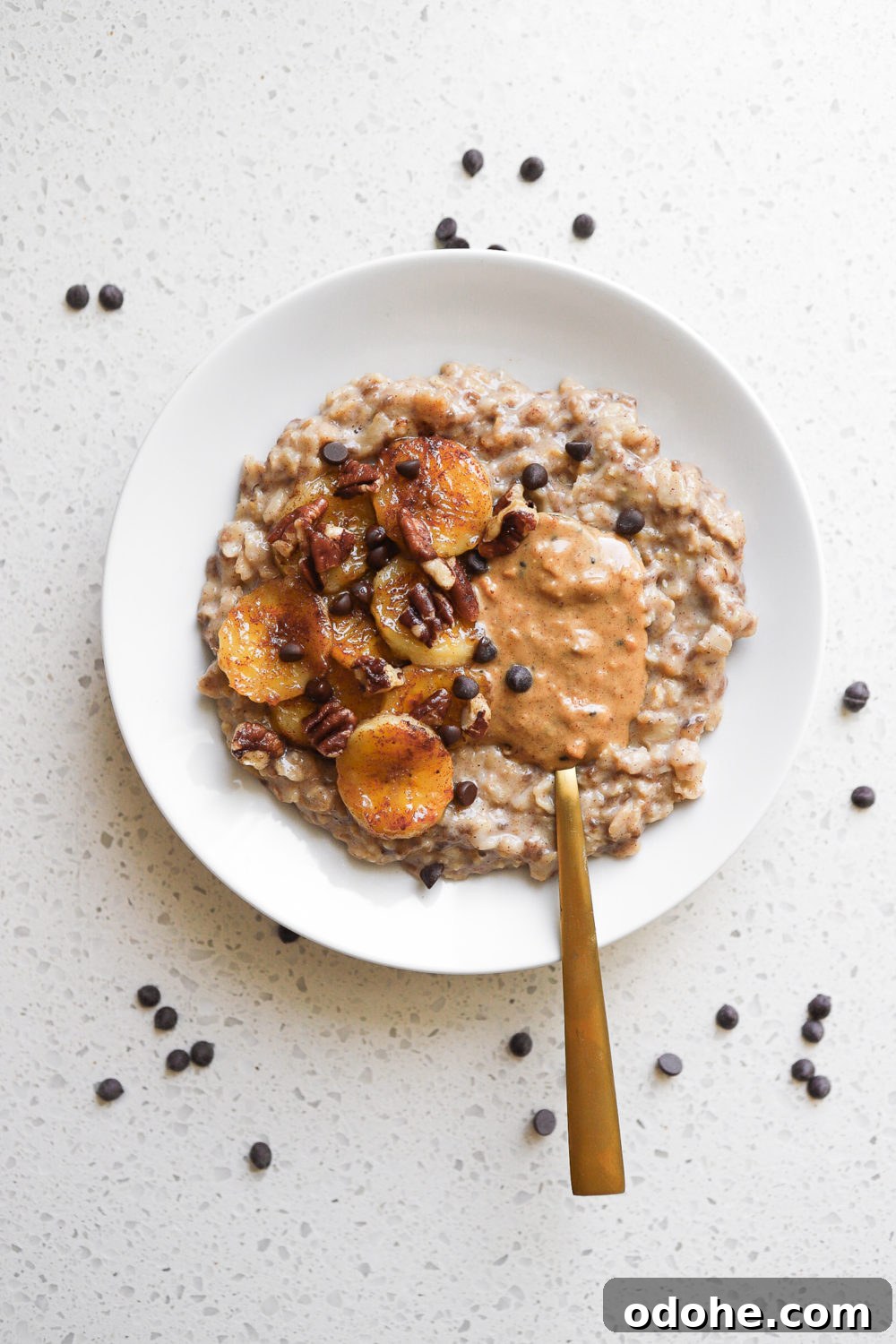 overhead shot of a bowl of banana bread oats topped with chocolate chips, caramelized bananas, nut butter and walnuts