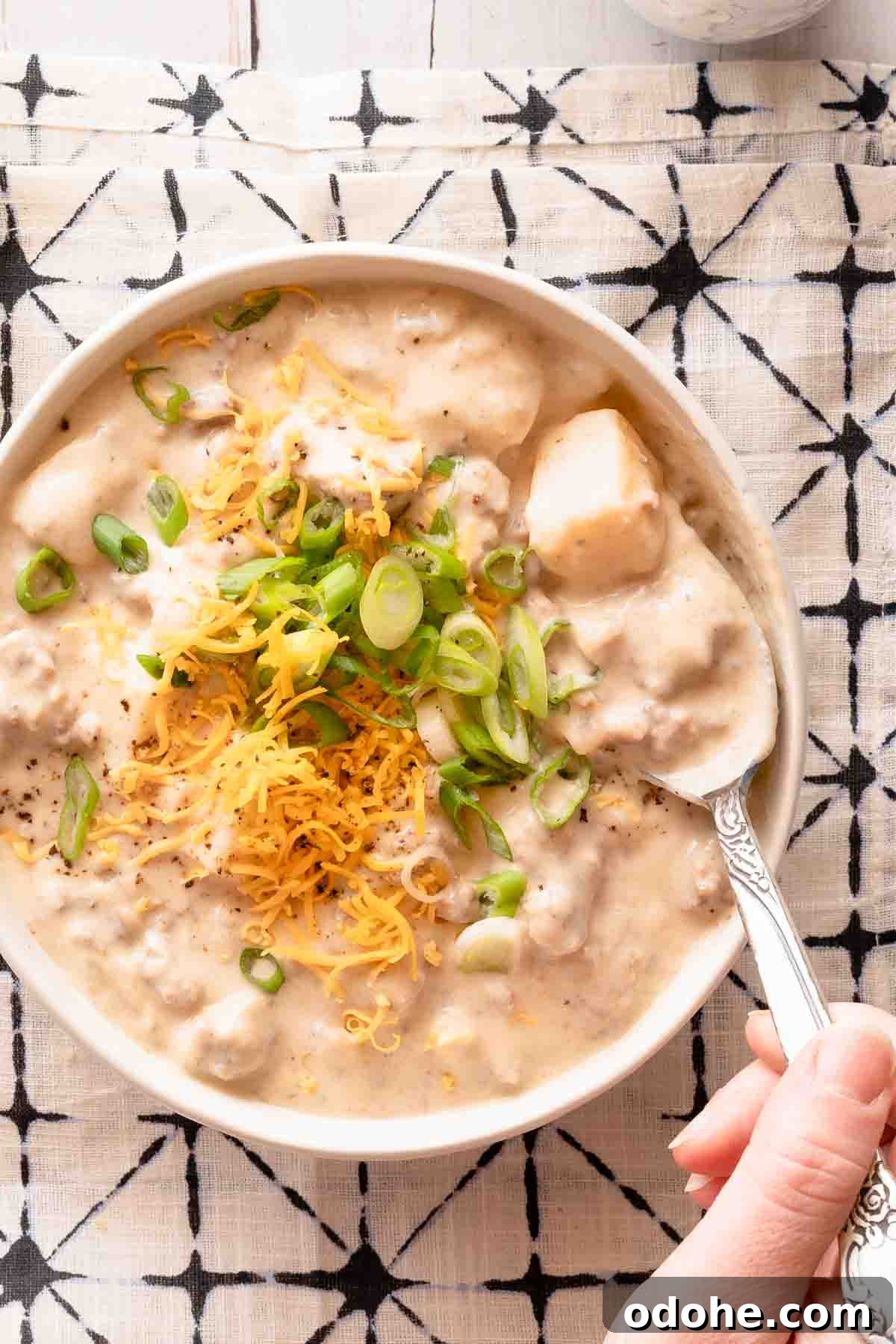 spoon dipping into bowl of creamy hamburger potato soup garnished with cheese and green onion.