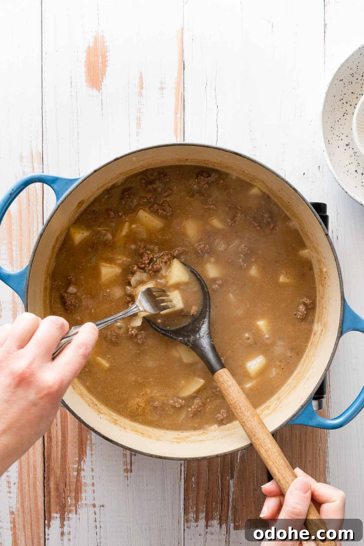 fork spearing a piece of potato overtop pot of soup.