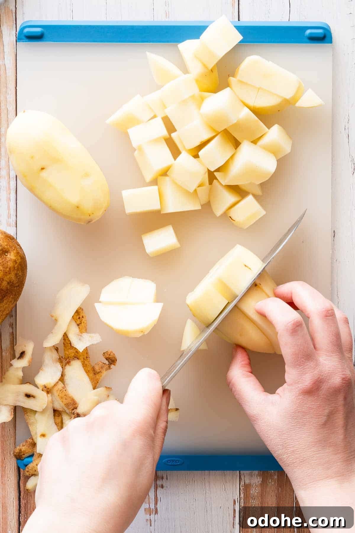 potatoes being cut into cubes on cutting board.