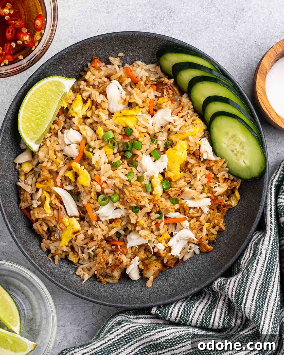 Plate of crab fried rice with side of lime wedges, sliced cucumbers and spicy fish sauce.