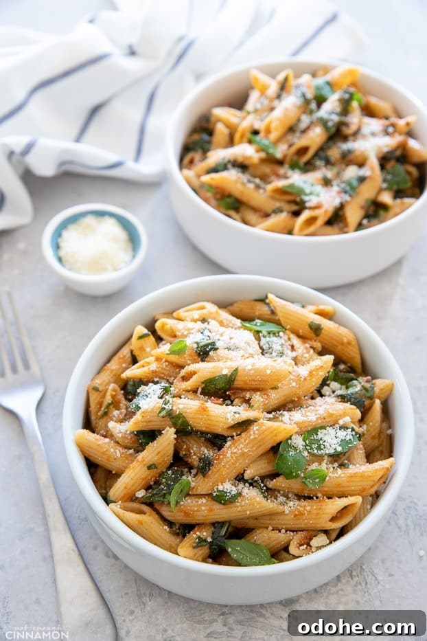 overhead shot of two small bowls with sun-dried tomato pasta with spinach, basil and parmesan cheese