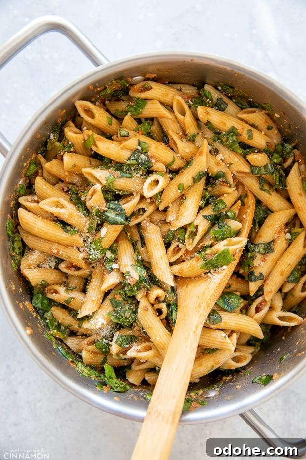 overhead shot of a pot with sun-dried tomato pasta with spinach and parmesan with a wooden spoon