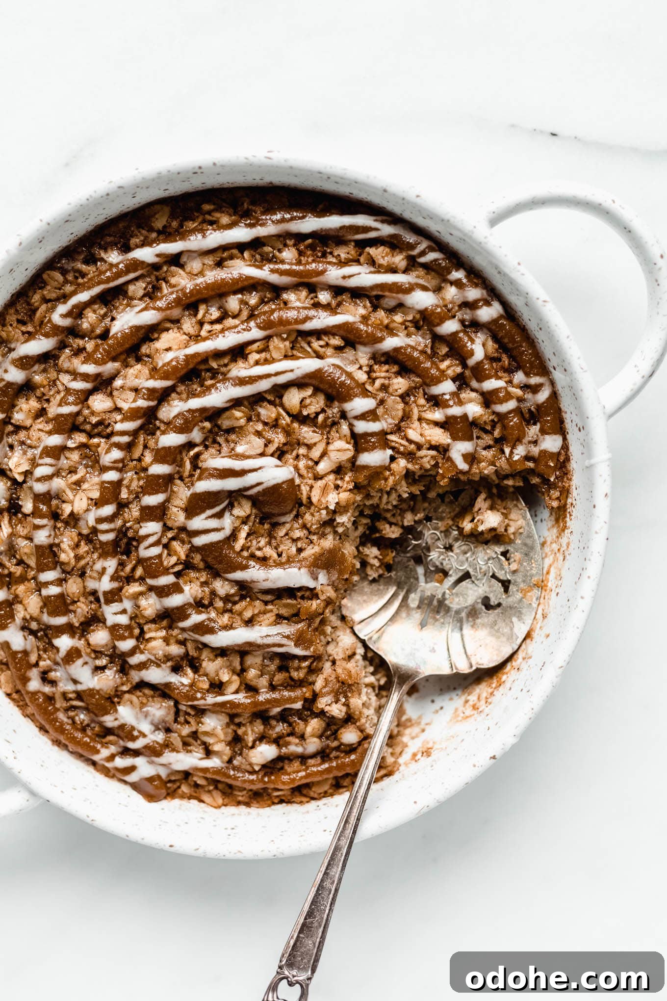 Cinnamon roll baked oats in a round white baking dish with a serving spoon in it.