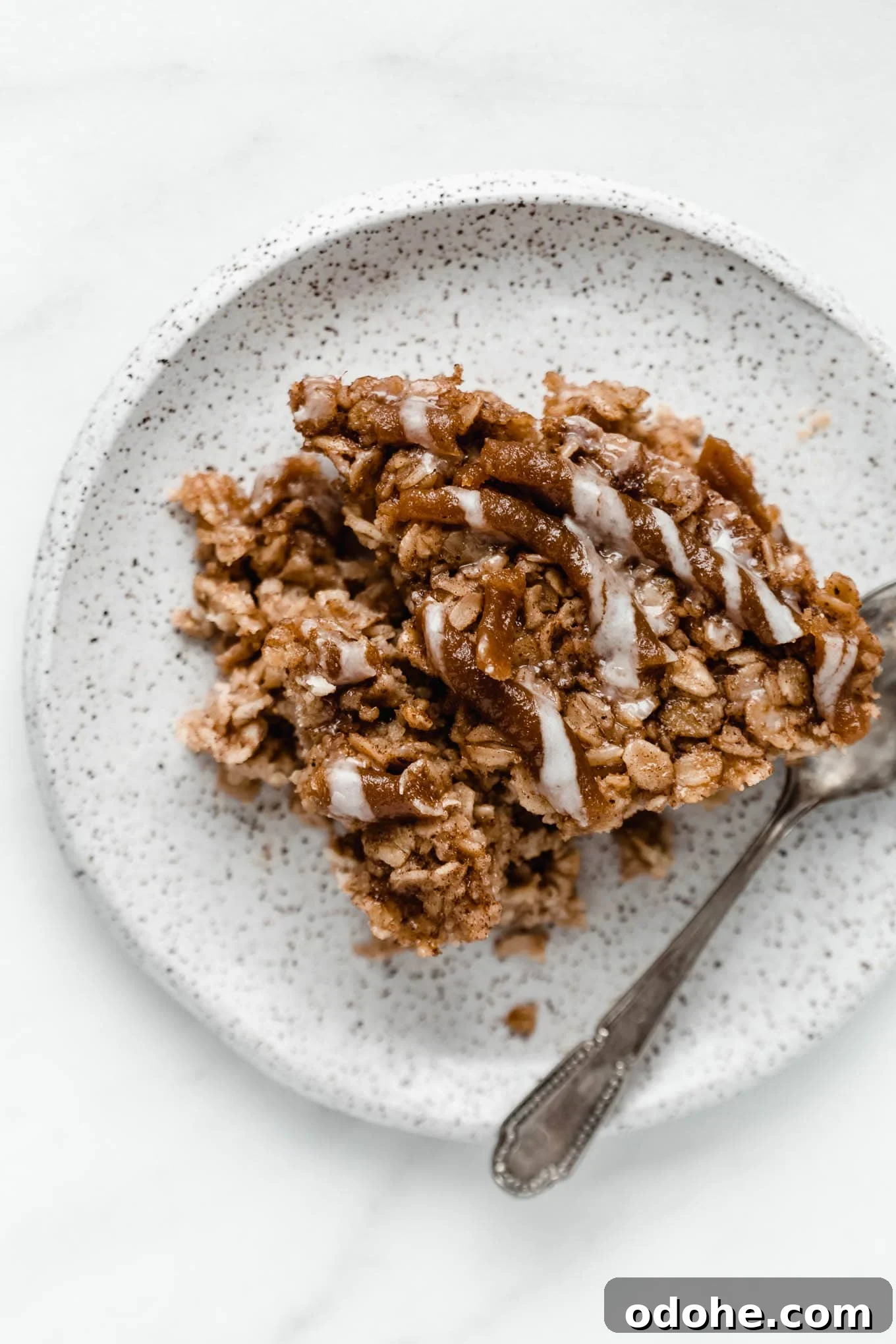 A slice of cinnamon roll baked oats on a white speckled plate.