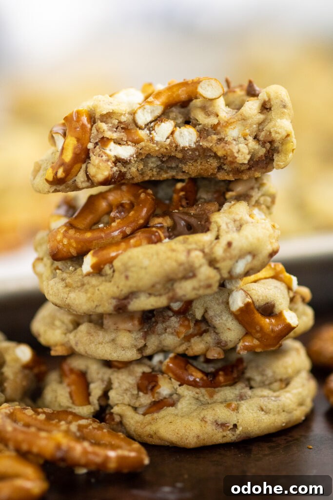 Salted Toffee Pretzel Cookies 2 Stack of four toffee pretzel cookies surrounded by pretzel twists with the baking sheet full of cookies in the background. The top cookie has a bite taken out.