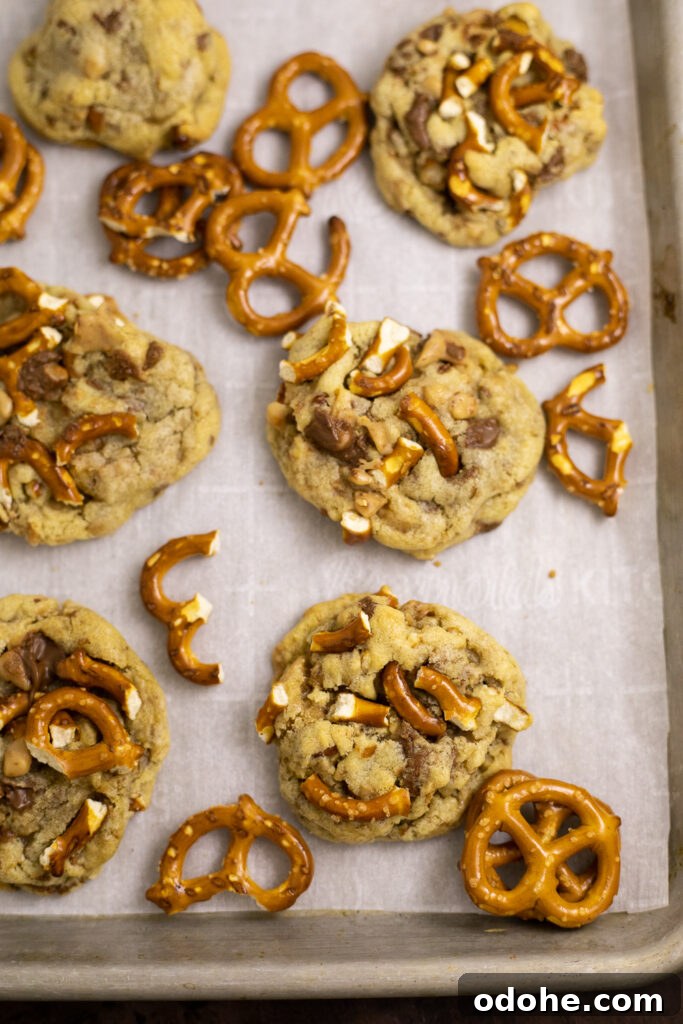 Salted Toffee Pretzel Cookies 3 Overhead view of a baking sheet lined with parchment paper with Toffee pretzel cookies and pretzels twists scattered on it.