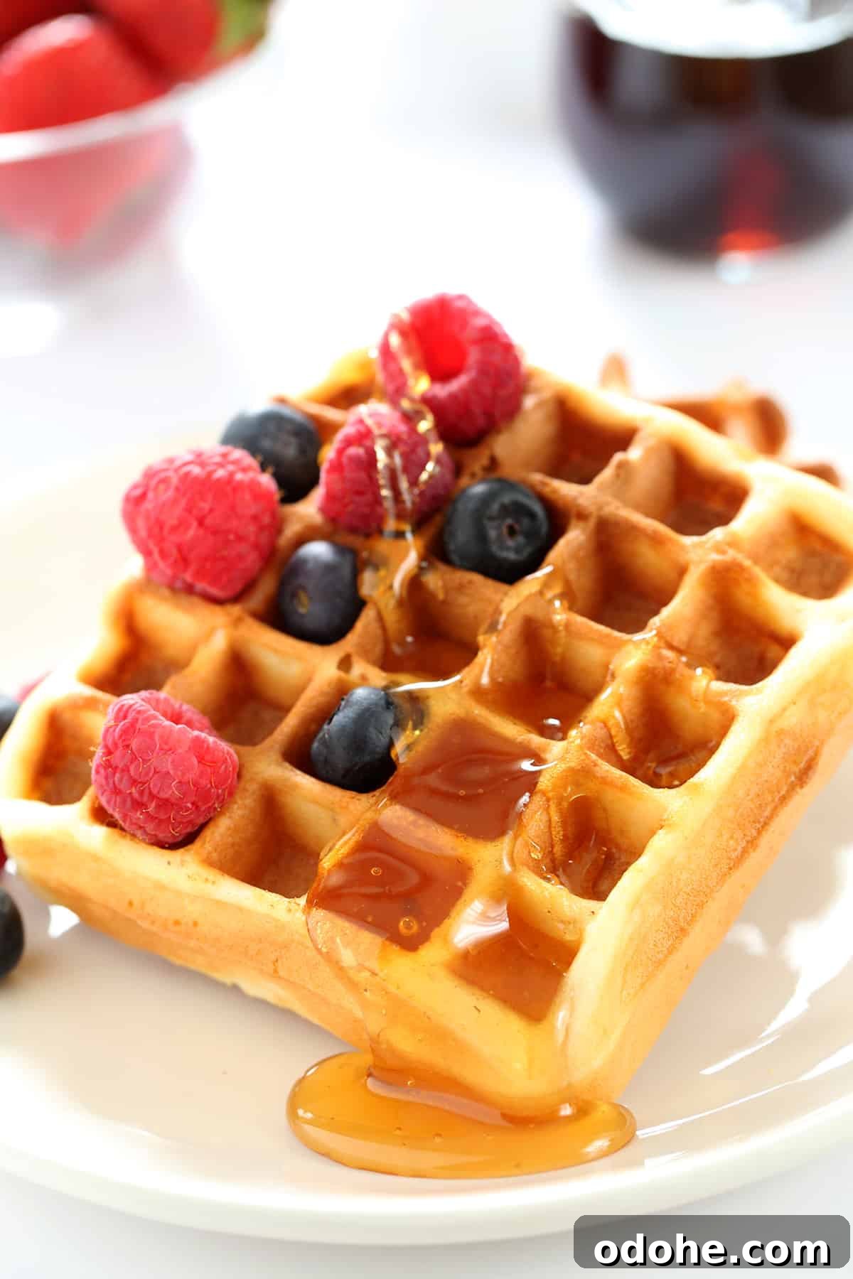 A close up of a waffle with raspberries, blueberries and syrup