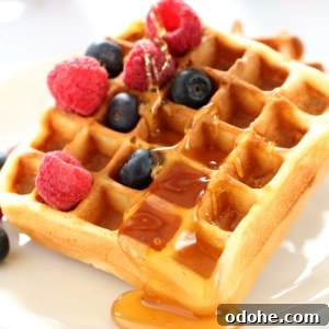 closeup of browned waffle with berries and syrup on a white plate