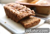 Small cutting board with a sliced loaf of banana bread and a baking dish with another loaf in the background