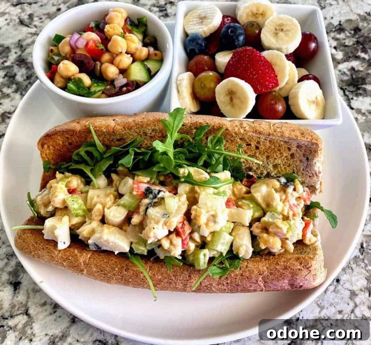 Hearts of Palm Vegan Lobster Roll Recipe 9 Vegan lobster roll recipe on a plate with fruit salad and chickpea salad.