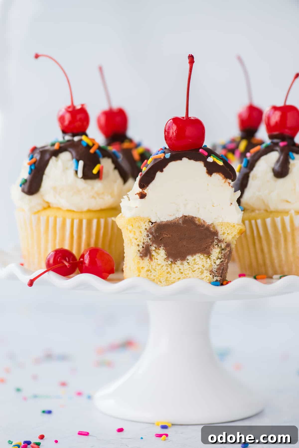 Ice Cream Cupcakes Recipe: Creamy No-Bake Dessert Cups 6 ice cream cupcakes with one cupcake cut in half showing chocolate ice cream center displayed on white cake stand on white background