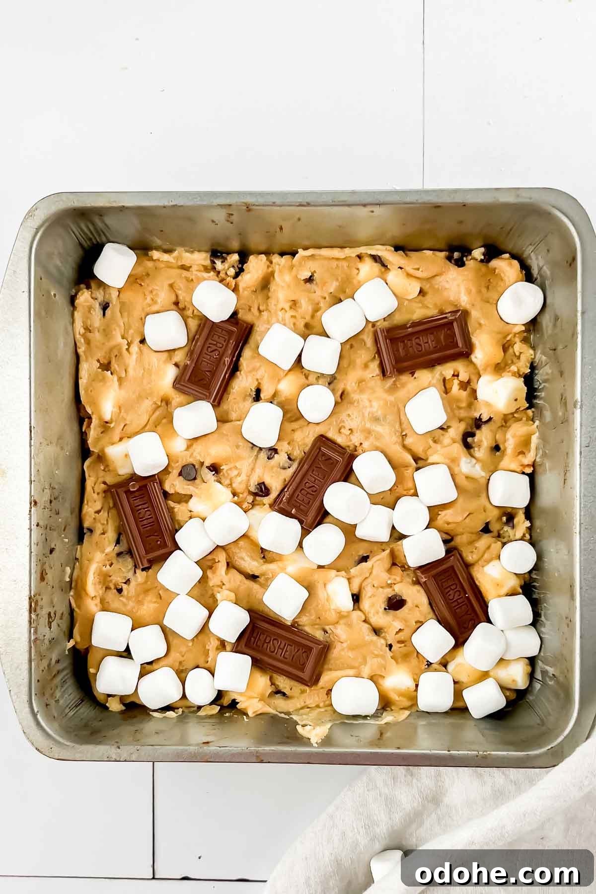 Smores casserole in square pan before baking topped with hersheys squares and marshmallows on top.