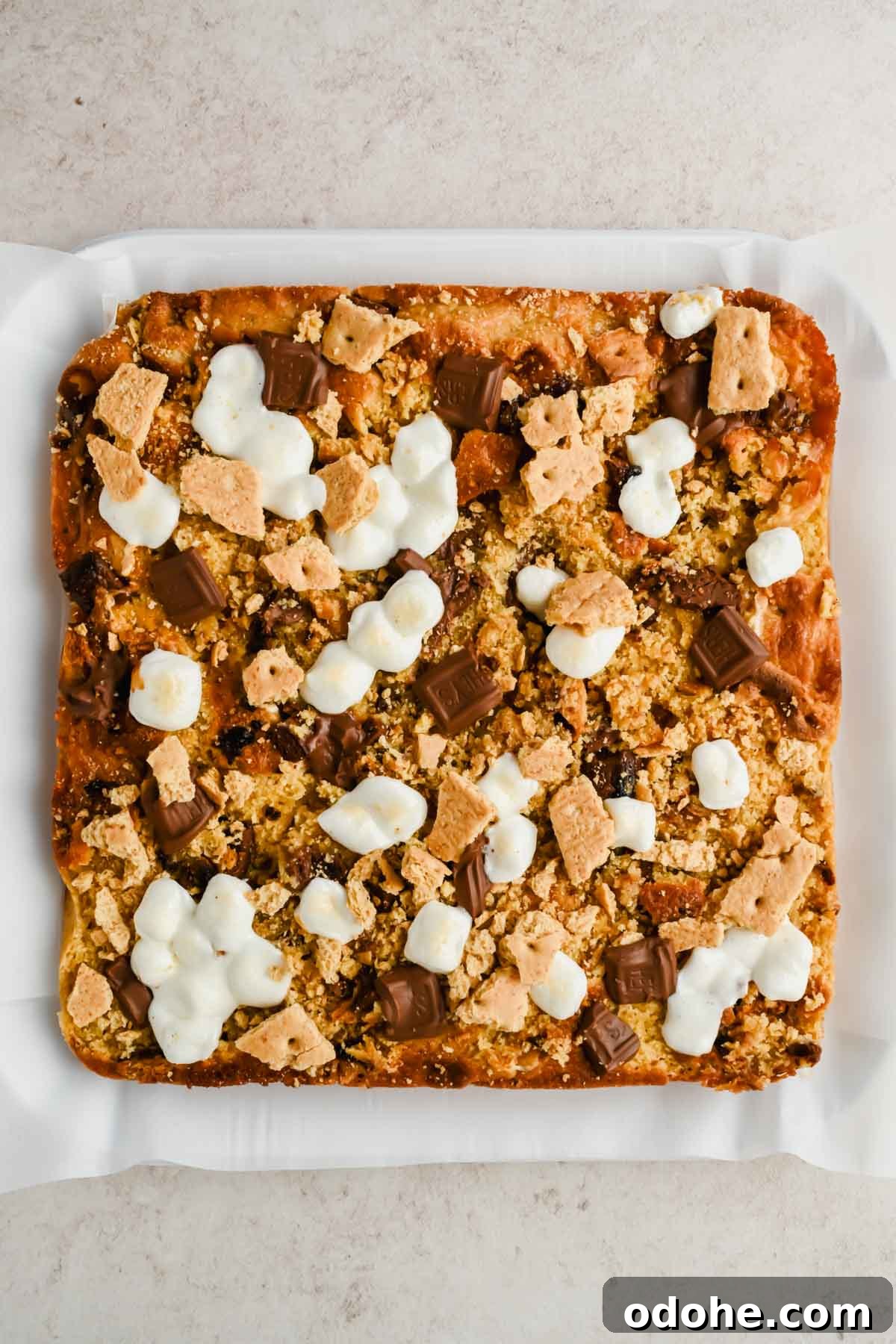 baked s'mores casserole topped with melted marshmallows, chunks of Hershey's and crushed graham crackers on parchment paper.