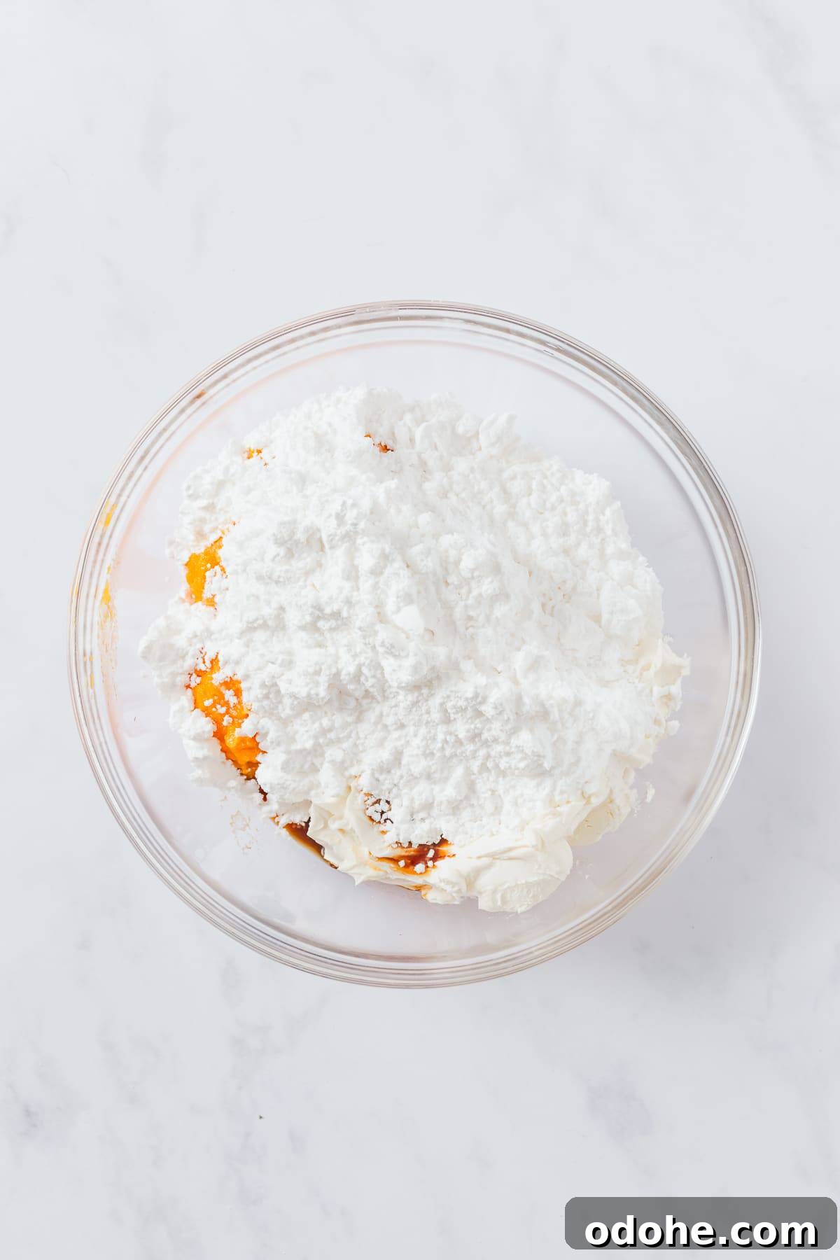 Strained pumpkin, cream cheese, powdered sugar, pumpkin pie spice, and vanilla added to a glass mixing bowl.