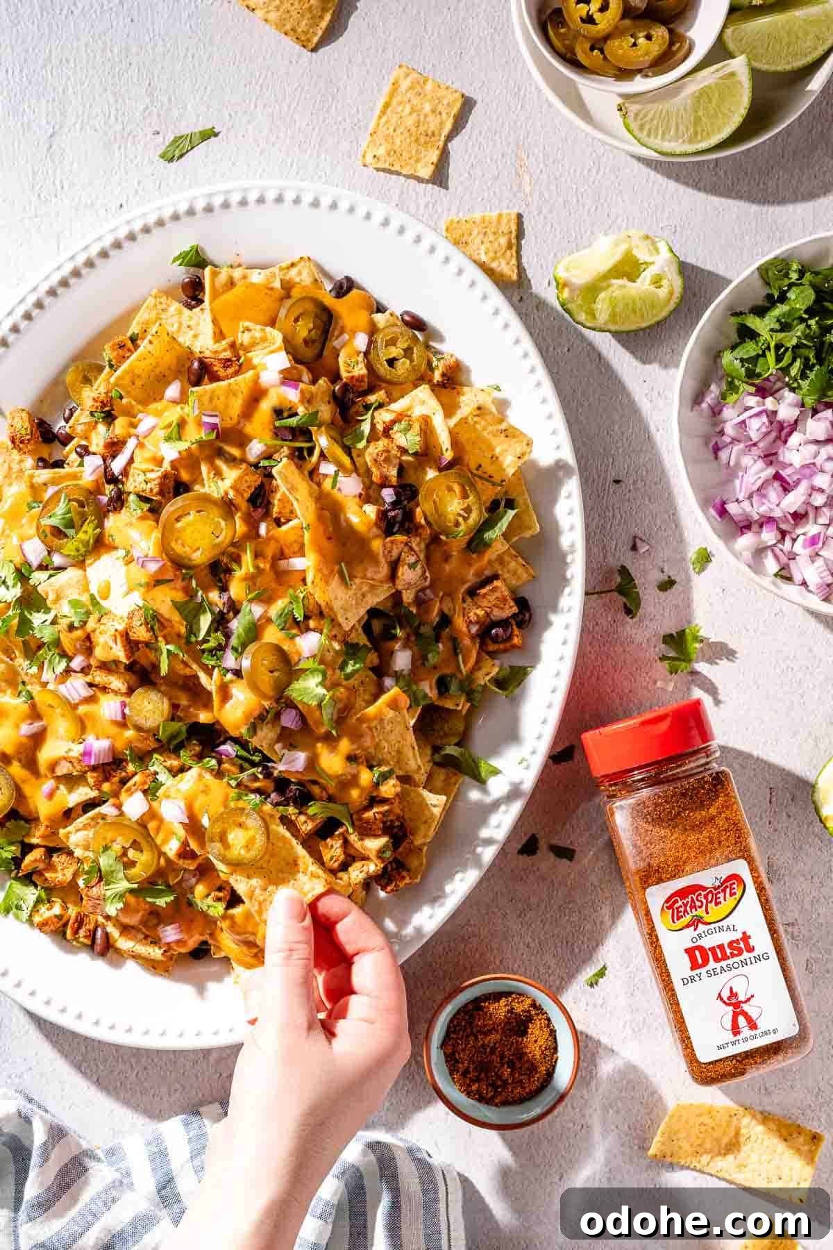 Crispy Spicy Queso Chicken Nachos Recipe 2 hand taking nacho from platter with toppings on the side